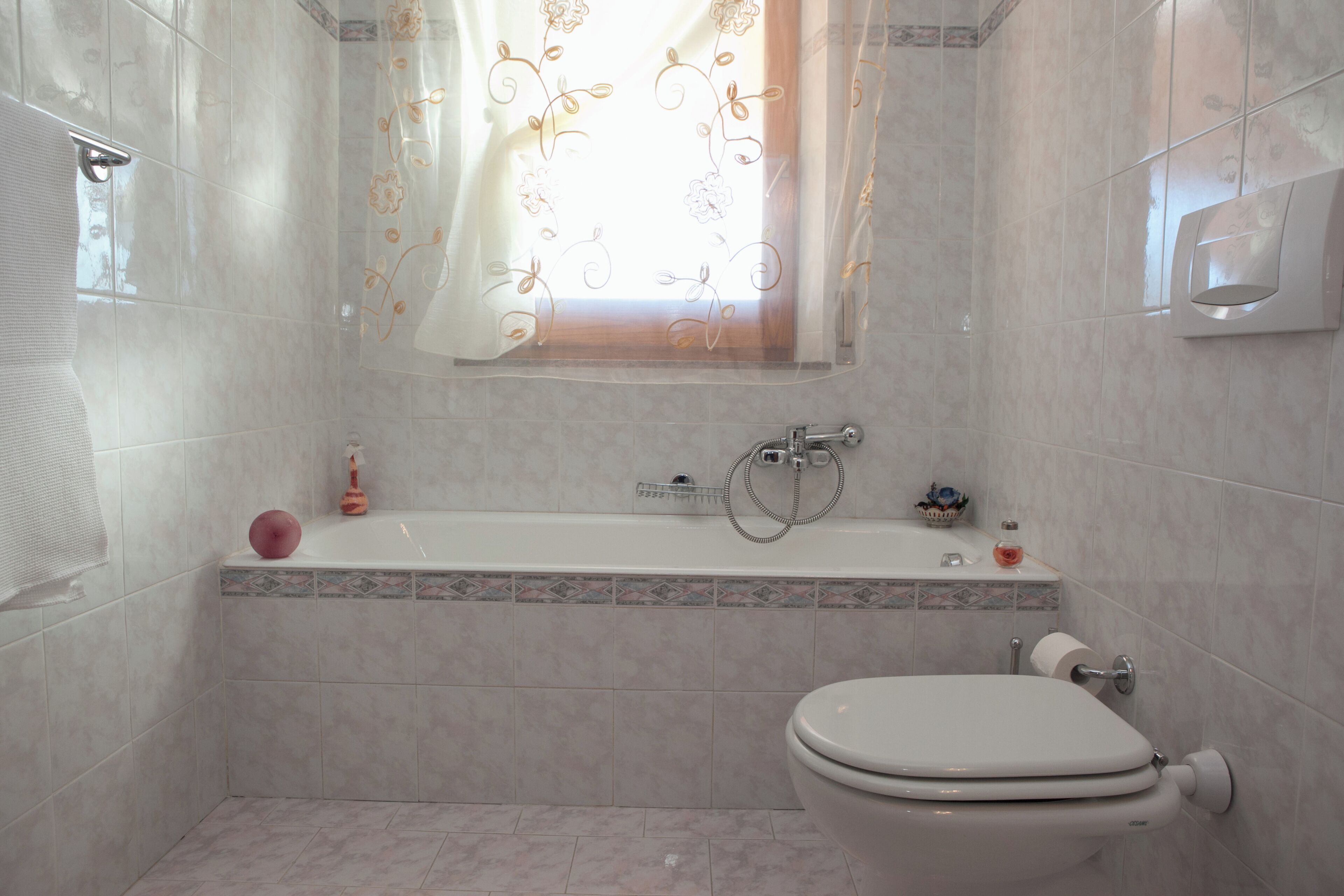 A bathroom with a bathtub, toilet, and a window with a floral curtain.