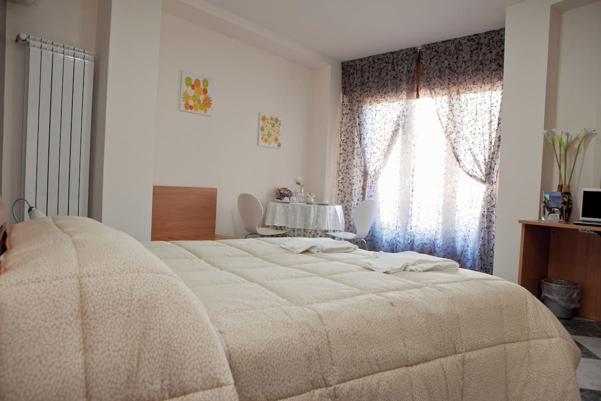 A bedroom with a large bed, a bedside table, a chair, a radiator, and a window with curtains.