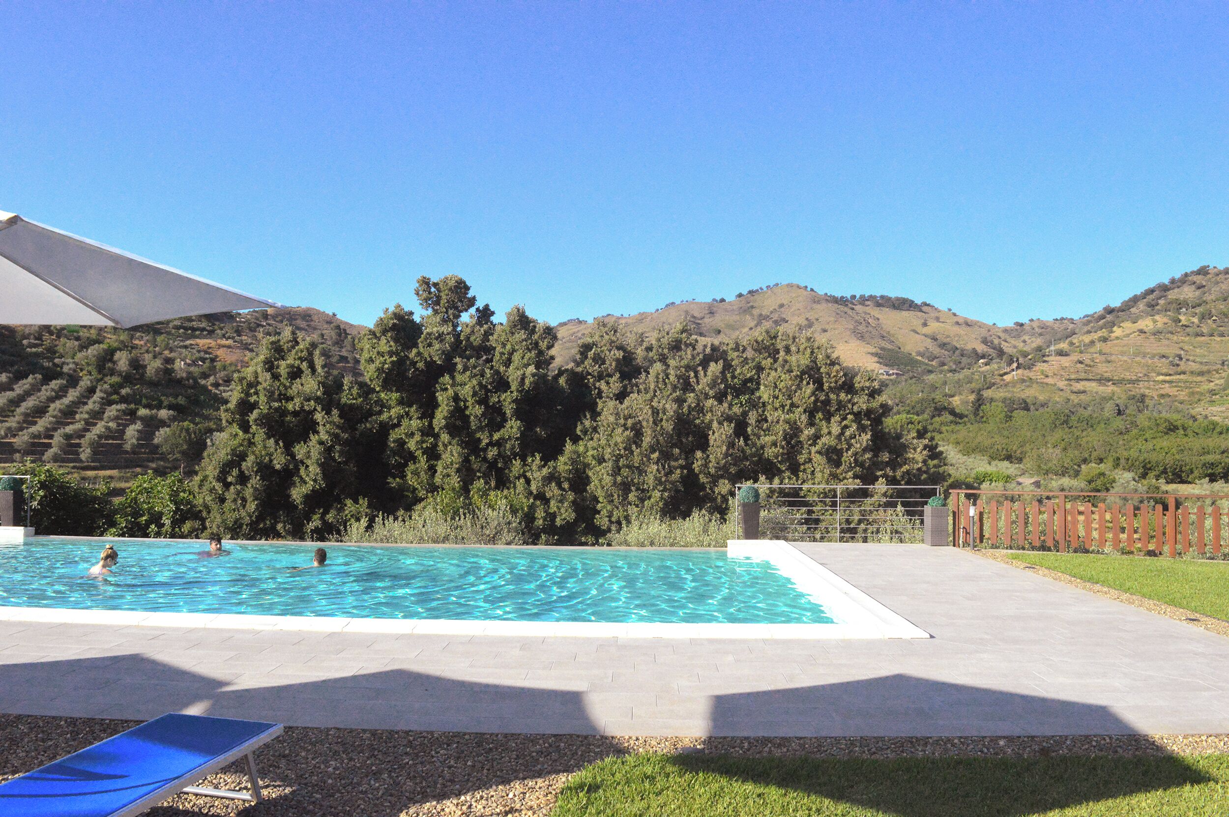 A rectangular swimming pool with clear blue water, surrounded by a concrete deck and a wooden fence.