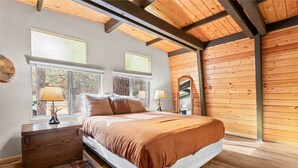 Ein Schlafzimmer mit einem großen Bett, zwei Fenstern, einer Holzbalkendecke und einem Nachttisch.