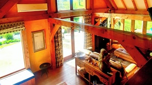 A rustic wooden interior with a loft bed, a fireplace, and a large arched window. - Streamside Country Manor - Peaceful Spacious Country Retreat Near Hobbiton (Richmond Downs)