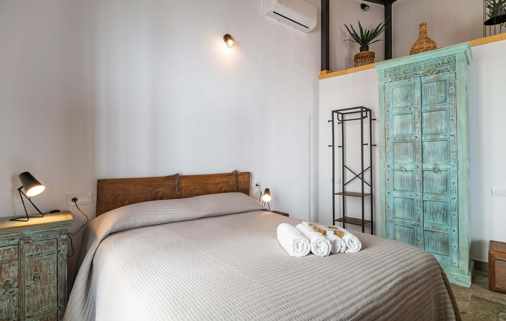 A bedroom with a bed, bedside lamps, a wardrobe, and an air conditioning unit.