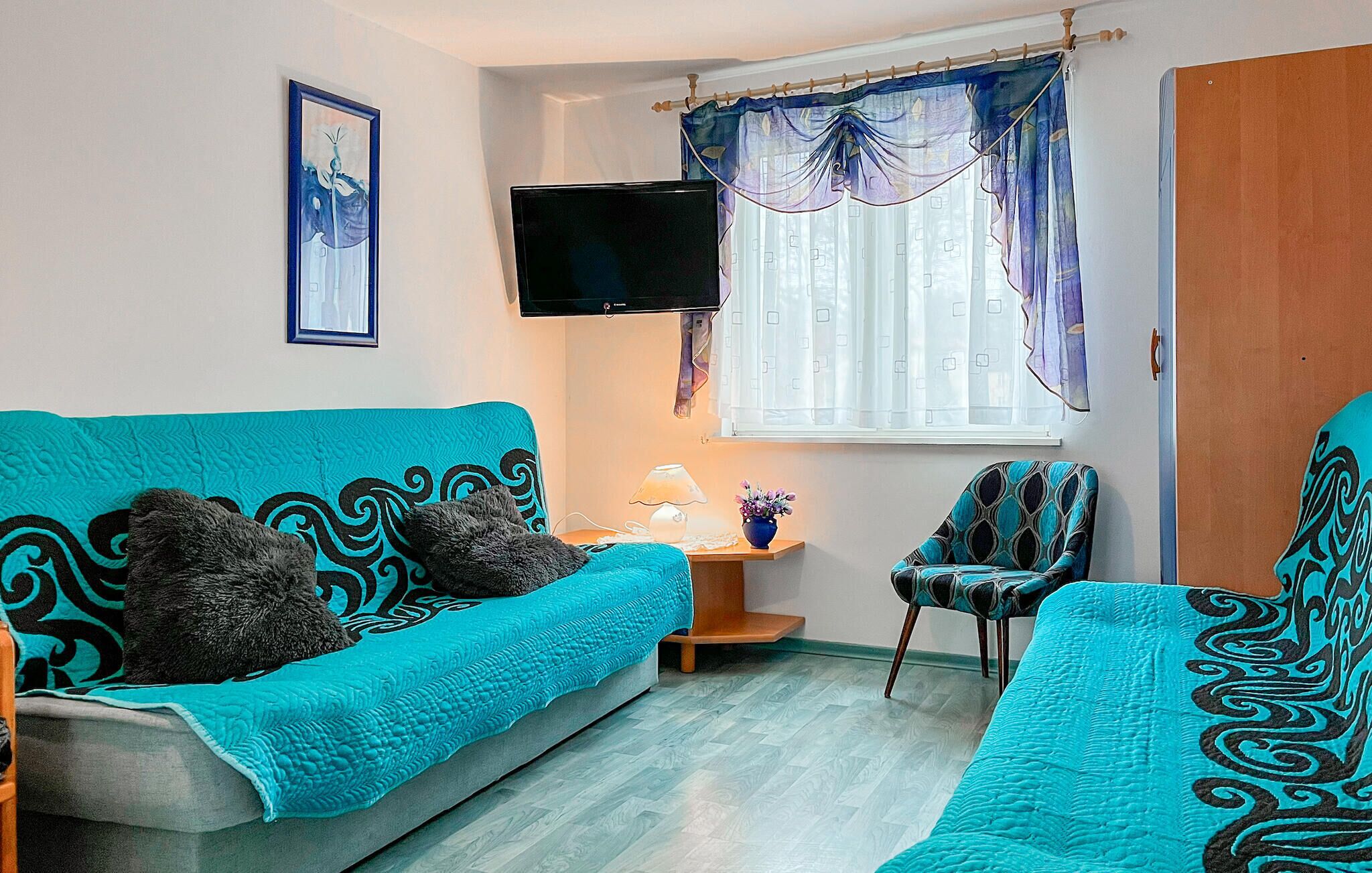 Una sala de estar con un sofá color turquesa, un sillón a juego y un televisor en la pared.