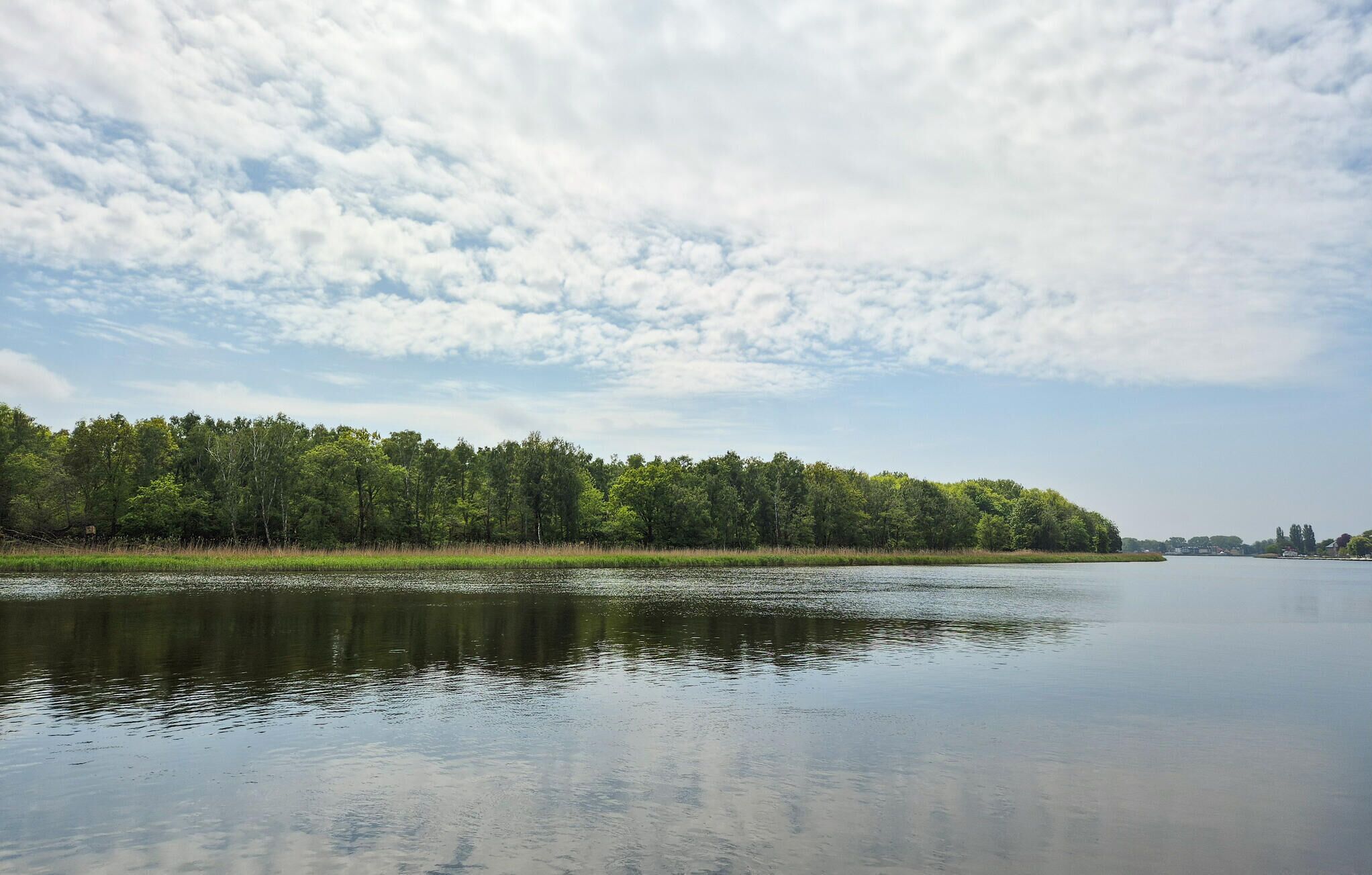 A calm lake with a forested shoreline and a partly cloudy sky.