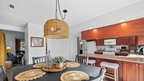 Eine moderne Küche mit Holzschränken, einer zentralen Kochinsel und einem Essbereich mit einem schwarzen Tisch und gewebten Platzsets.