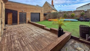 A wooden deck with a grassy lawn, a stone wall, and a small inflatable pool. - 4 bedroom nice home in Penvénan (Penvénan)