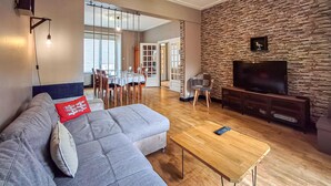 A living room with a grey sofa, a wooden coffee table, and a flat-screen TV on a stone wall. - 4 bedroom nice home in Penvénan (Penvénan)