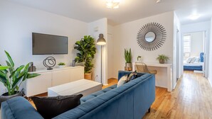 A modern living room with a blue sofa, a flat-screen TV, a round mirror, and a desk with a chair. - Stylish Plateau Getaway | Steps from Mont-Royal (Montréal)