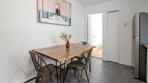 A dining area with a wooden table, metal chairs, a vase with dried flowers, a painting on the wall, and a refrigerator. - Stylish Plateau Getaway | Steps from Mont-Royal (Montréal)