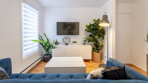 A modern living room with a flat-screen TV, a white cabinet, a blue sofa, and a potted plant. - Stylish Plateau Getaway | Steps from Mont-Royal (Montréal)