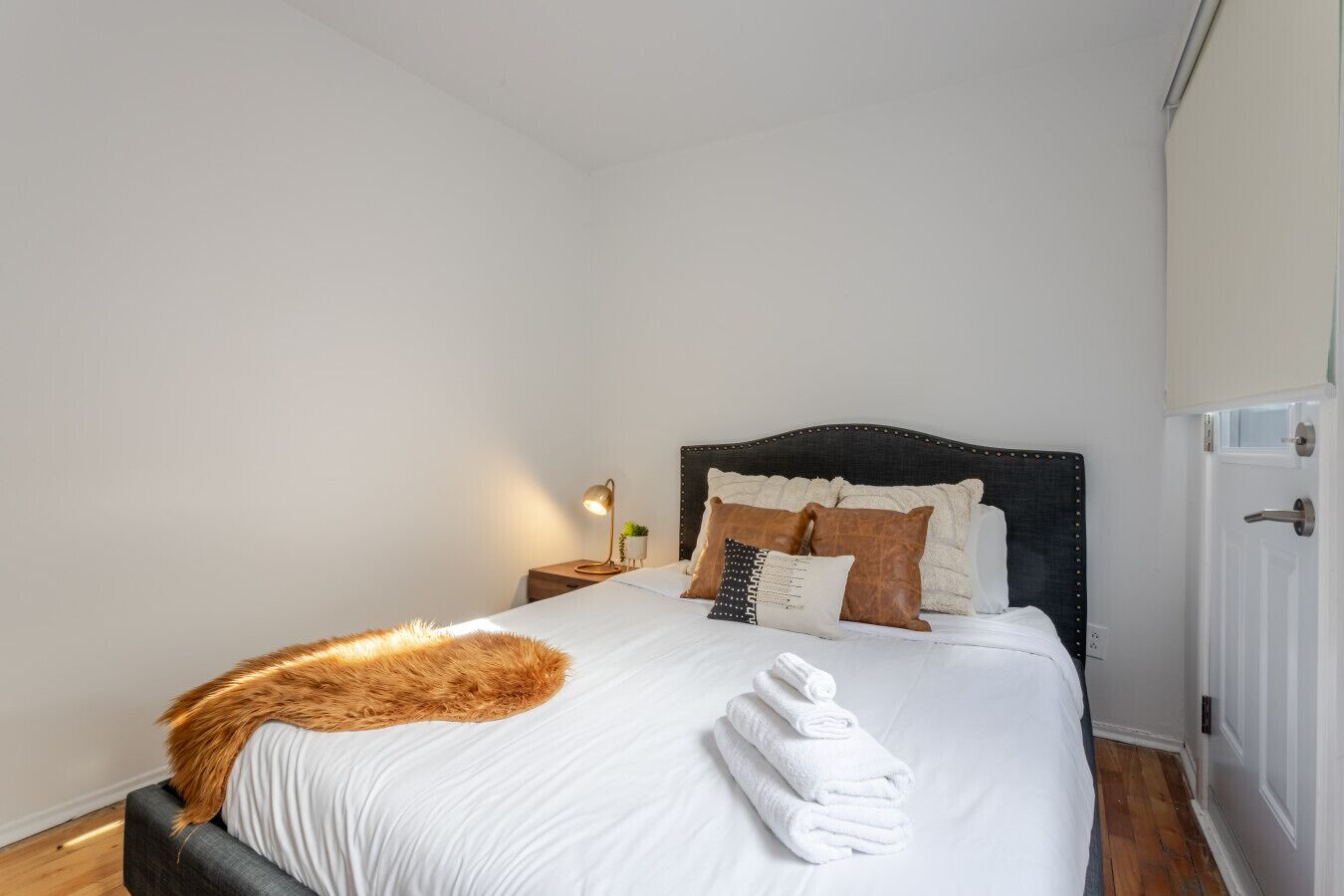 A neatly made bed with white linens, a fur throw, and several pillows.