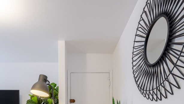 A modern living room with a white sofa, a floor lamp, a TV, and a decorative mirror. - Stylish Plateau Getaway | Steps from Mont-Royal (Montréal)