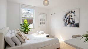 A bedroom with a bed, a window, a door, a painting, and a plant. - Modern 2BR in Plateau – Steps to Downtown (Montréal)
