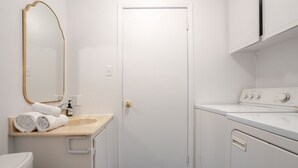 A small, clean laundry room with a washing machine, a sink, and a door. - Modern 2BR in Plateau – Steps to Downtown (Montréal)
