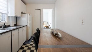 A compact kitchen with white cabinets, a black and white checkered floor, and a dining area with a long table and chairs. - Modern 2BR in Plateau – Steps to Downtown (Montréal)