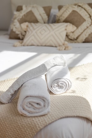 A neatly made bed with rolled white towels and a beige blanket, accompanied by patterned pillows. - Modern 2BR in Plateau – Steps to Downtown (Montréal)