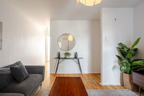 A modern living room with a grey sofa, a wooden coffee table, a round mirror, and a potted plant.