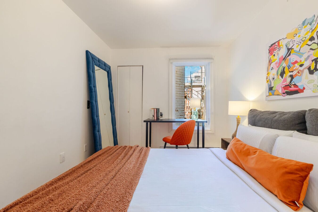 Un dormitorio con cama, escritorio, silla, ventana y un cuadro en la pared.