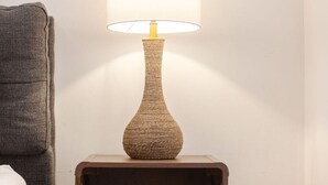 Een nachtkastje met een lamp, een lade en een stoel.