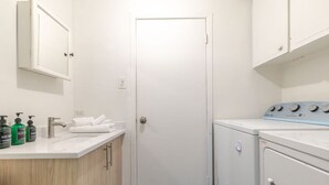 Een kleine wasruimte met een wasmachine, een wastafel met toiletartikelen en een deur.