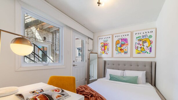 Een slaapkamer met een bed, een bureau, een stoel, een raam en drie Picasso kunstwerken aan de muur.