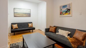 Un salon avec un canapé noir, une table basse et deux tableaux accrochés au mur.