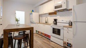 Une cuisine moderne avec des meubles blancs, une table en bois et deux tabourets de bar.