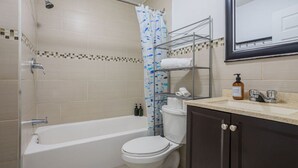 A bathroom with a bathtub, toilet, and a shower curtain with a fish pattern. There is a shelf with towels and toiletries. - Spacious & Trendy 2BR – Heart of Montreal (Montréal)