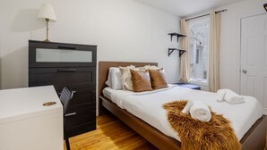 A bedroom with a bed, a dresser, a lamp, a window with curtains, and a door. - Spacious & Trendy 2BR – Heart of Montreal (Montréal)