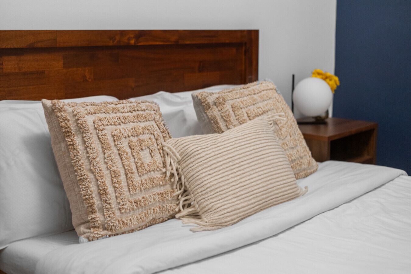 Ein Bett mit Holz-Kopfstück, zwei gemusterten Kissen und einer weißen Decke.
