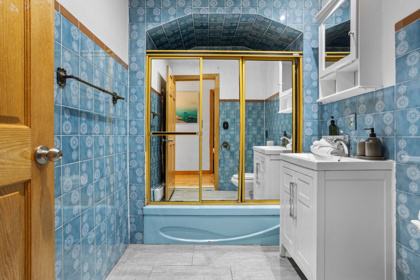 Un baño con baldosas azules estampadas, una bañera, una cabina de ducha y un lavamanos con artículos de aseo.