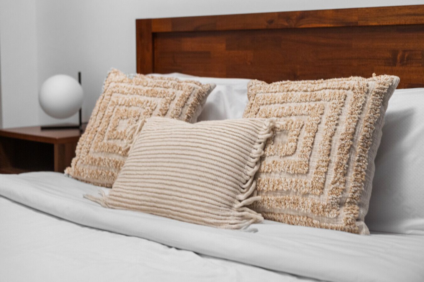 A bed with a wooden headboard, two textured pillows, and a white bedside table with a spherical object.