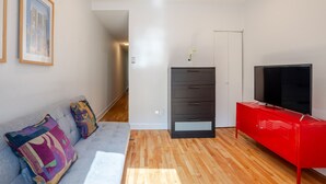 A modern living room with a grey sofa, colorful cushions, a red cabinet, a flat-screen TV, and a grey filing cabinet.