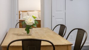 A dining table with four chairs, a potted plant with white flowers, and a white door in the background.