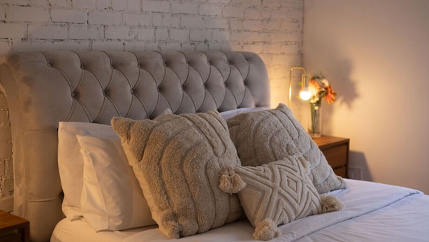Ein ordentlich bezogenes Bett mit einer gebügelten Kopfteil, zwei Zierkissen und ein Nachttisch mit Lampe und Blumen.