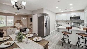 A modern kitchen with a stainless steel refrigerator, white cabinetry, and a bar area with stools.