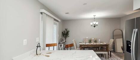 A modern kitchen with a marble island, wooden chairs, a dining table, and a refrigerator.