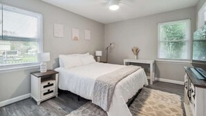 A bedroom with a bed, bedside tables, a ceiling fan, and windows with blinds.