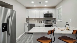 A modern kitchen with white cabinets, stainless steel appliances, and a marble island with bar stools.