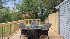 A deck with wicker furniture and a glass table, surrounded by a wooden fence and trees.