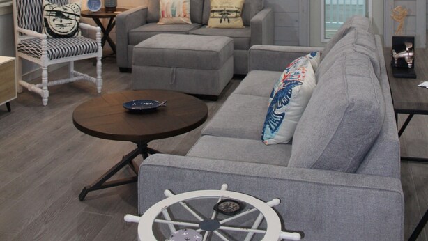 A spacious living room with a high ceiling, a ceiling fan, a grey sofa, a round coffee table, and a white armchair.