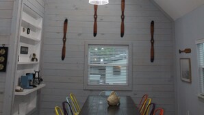 A dining area with a wooden table, colorful chairs, pendant lights, and a window with blinds.