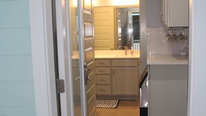 A narrow hallway leading to a kitchen with a welcome mat, wooden flooring, and a sink area.