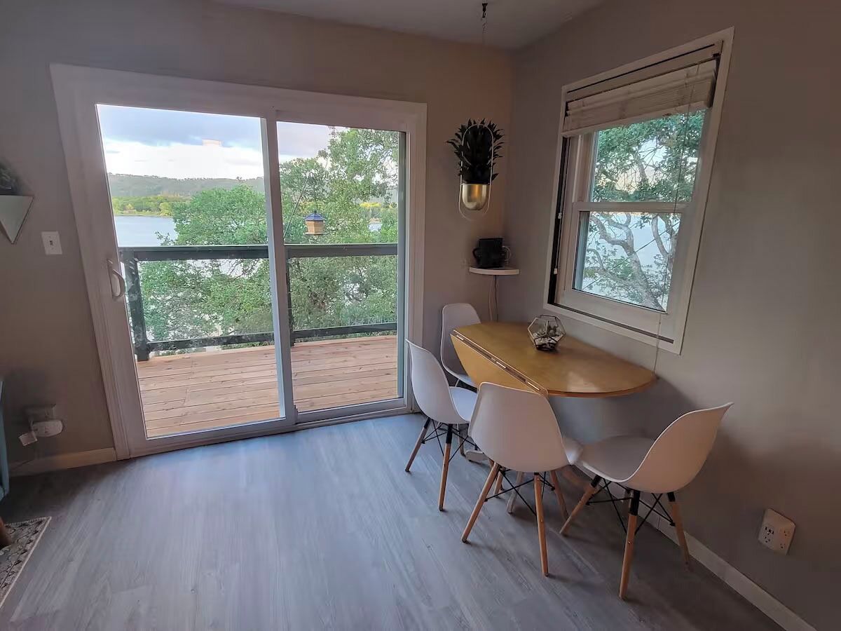 A dining area with a round table and four chairs, a sliding glass door leading to a balcony, and a potted plant on the wall.