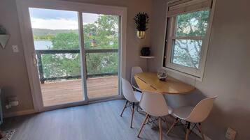 A dining area with a round table and four chairs, a sliding glass door leading to a balcony, and a potted plant on the wall.