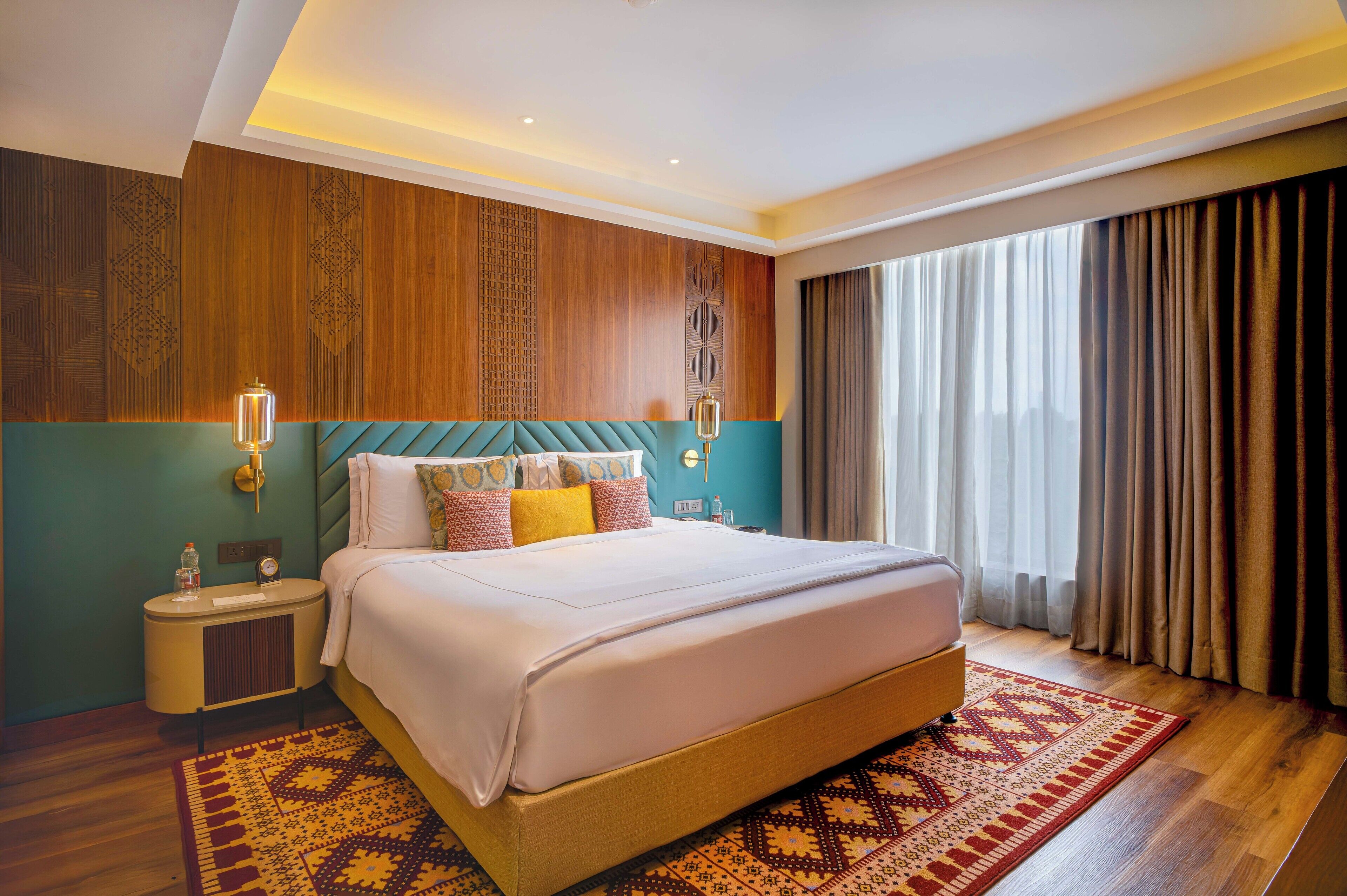 A large bed with a headboard, a bedside table, a nightstand, and a patterned rug.