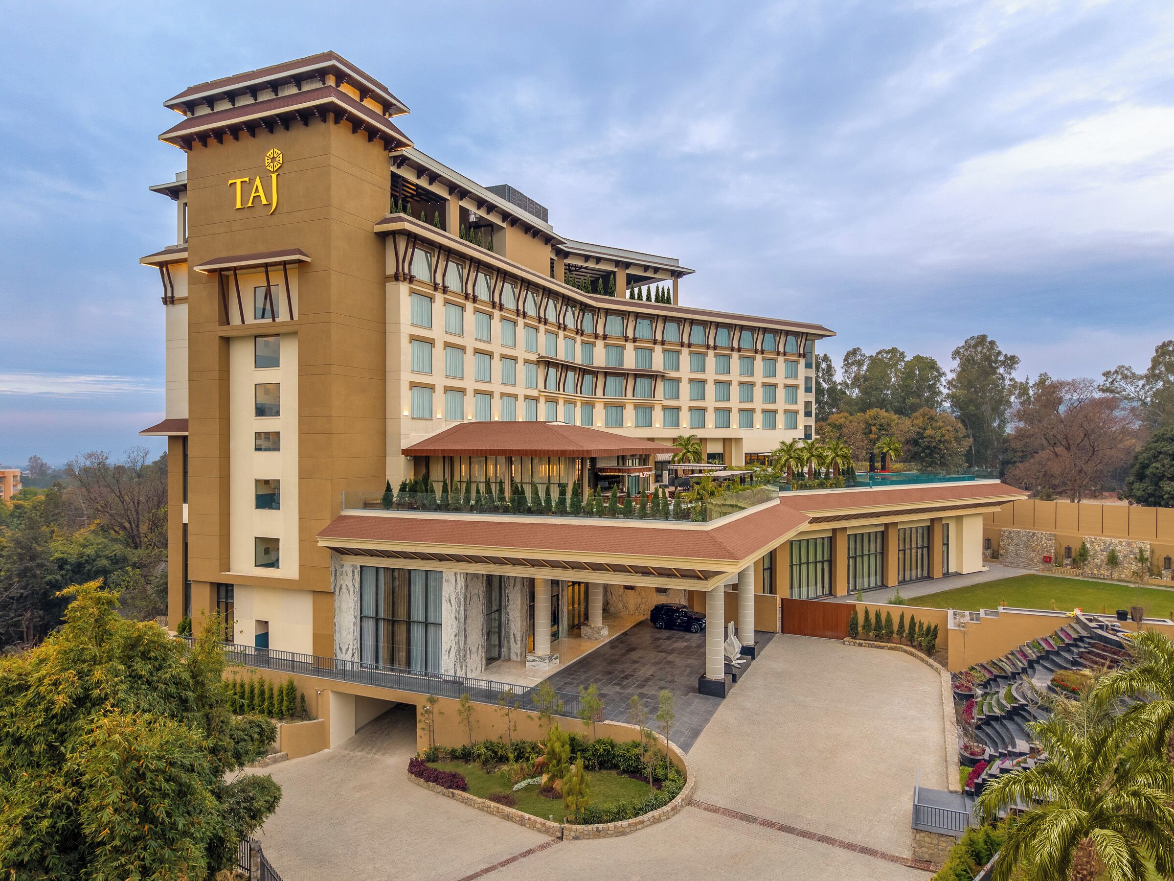 Un hotel con un llamativo letrero 'TAJ', una amplia piscina al aire libre y un patio ajardinado.