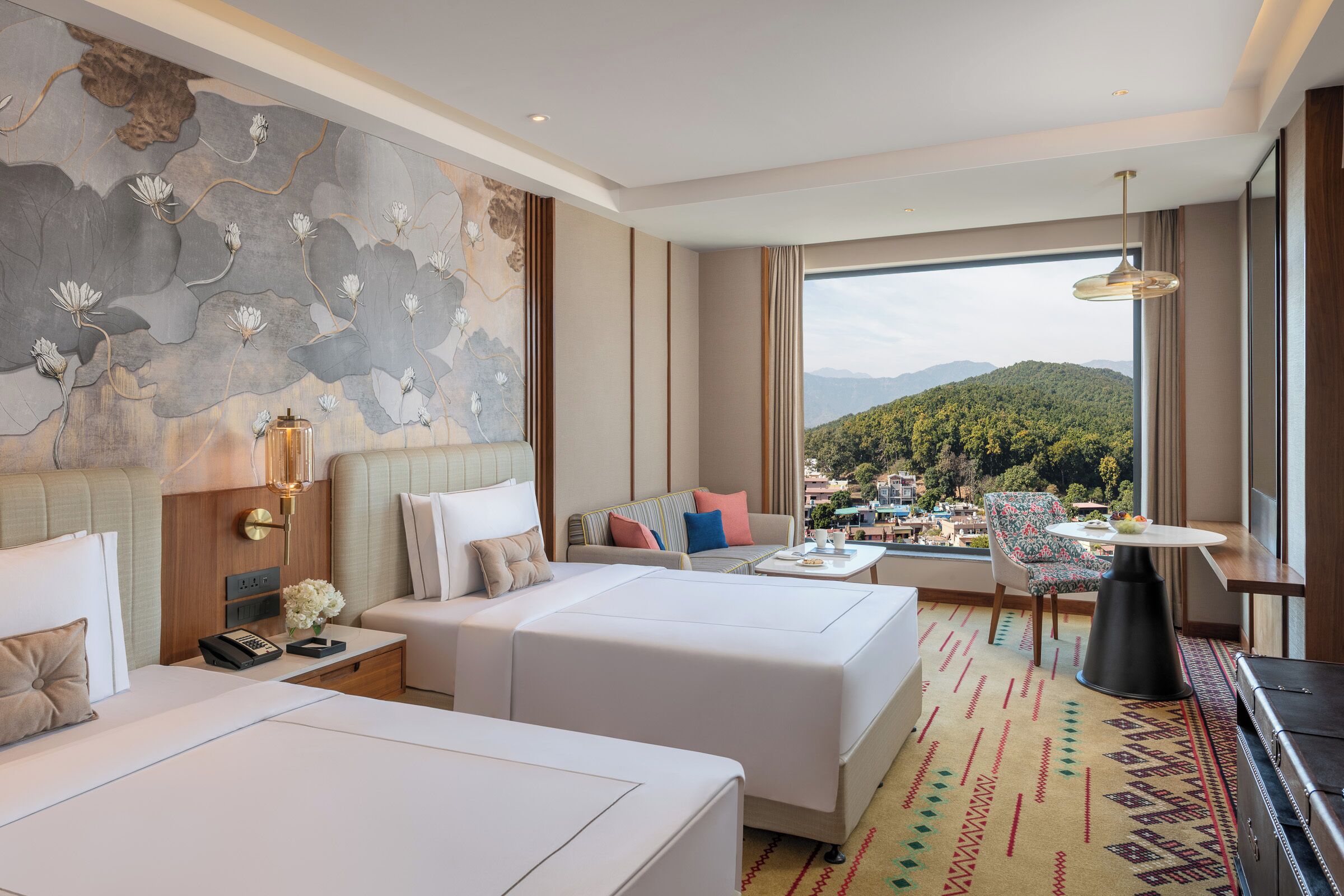 A hotel room with two beds, a sofa, a dining table, and a view of a mountainous landscape.