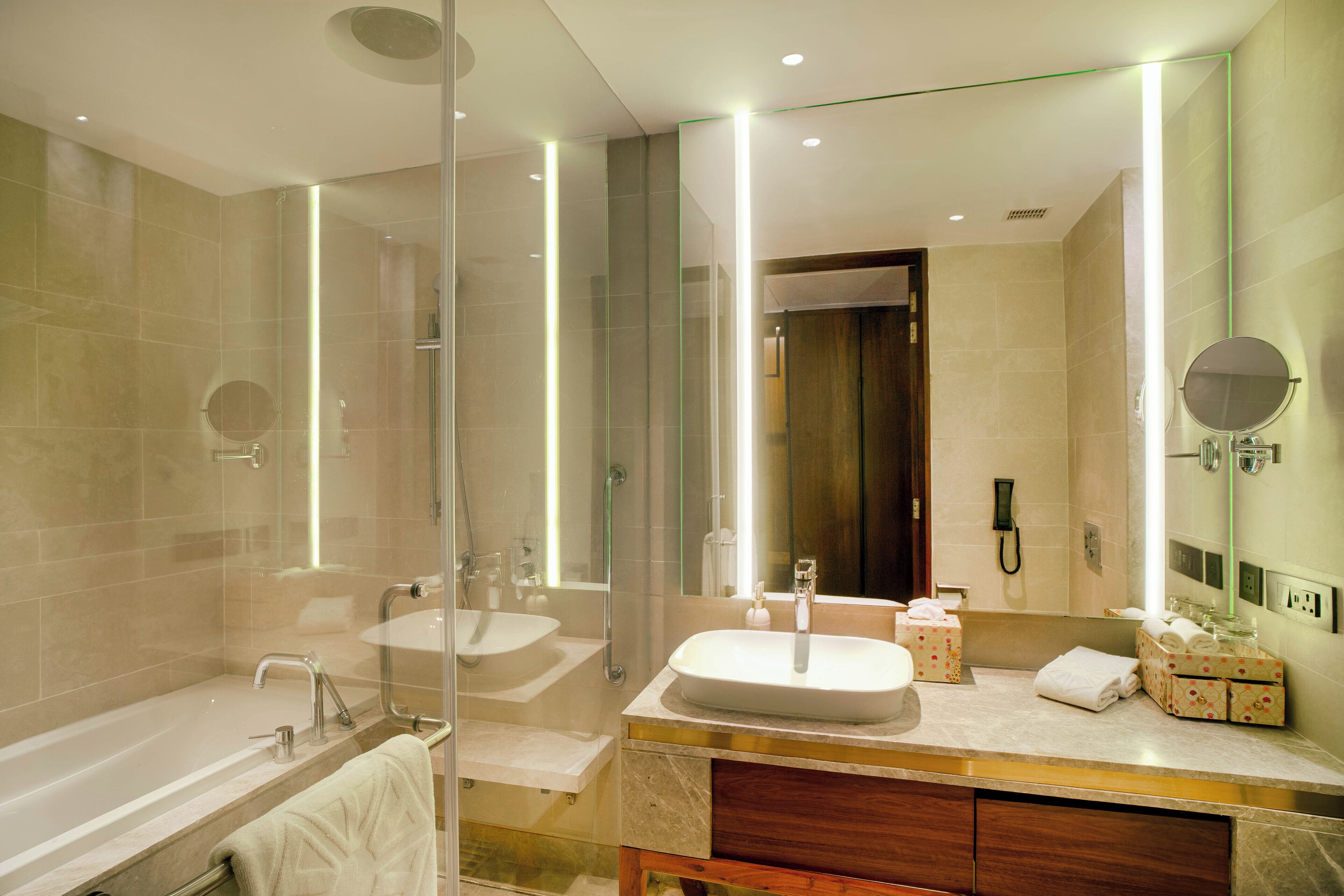 A modern bathroom with a glass-enclosed shower, two sinks, a vanity with a mirror, and a bathtub.