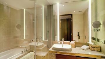 A modern bathroom with a glass-enclosed shower, two sinks, a vanity with a mirror, and a bathtub.